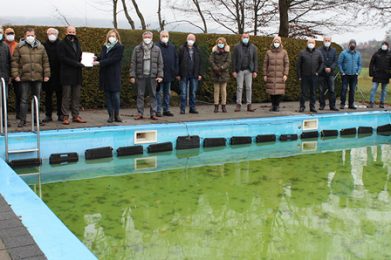 Große Freude in Bad Soden-Salmünster-Mernes: Aus Mitteln der Dorfentwicklung in Höhe von 565.000 Euro kann das Quellenbad in ein Naturbad umgebaut werden. Den Förderbescheid überbrachte Katrin Hess, Leiterin des Amtes für Umwelt, Naturschutz und ländlicher Raum (Neunte von links), an Bürgermeister Dominik Brasch (Achter von links) im Beisein von Vertretern der städtischen Gremien, dem Ortsbeirat und ehrenamtlichen Helferinnen und Helfern, die sich seit Jahren um den Erhalt des kleinen Bades bemühen.