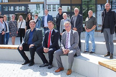 Kreisbeigeordneter und Schuldezernent Winfried Ottmann (vorne rechts), Schulleiter Andreas Leibold (vorne links) und Bürgermeister Matthias Möller (vorne Mitte) nehmen auf den Sitzflächen des neu gestalteten Schulhofs Platz. Im Hintergrund das Gebäude, in dem die neue Mensa sowie Räume für Musik, Physik, Biologie und Chemie untergebracht sind.