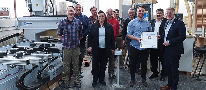 Im Kreise der Mitarbeitenden der Hehl Gmbh | Schenk1918 überreichten Kreisbeigeordneter Winfried Ottmann (rechts) und Walter Dreßbach (Zweiter von rechts), Leiter des Referats für Wirtschaft, Arbeit und digitale Infrastruktur, Julian und Uwe Hehl (Dritter und Vierter von rechts), Geschäftsführer beziehungsweise Gesellschafter des Unternehmens, das Siegel „Made in Main-Kinzig“. Bei der Übergabe war auch Jürgen Schenk (Dritter von links), vormaliger Inhaber der Schreinerei, anwesend.